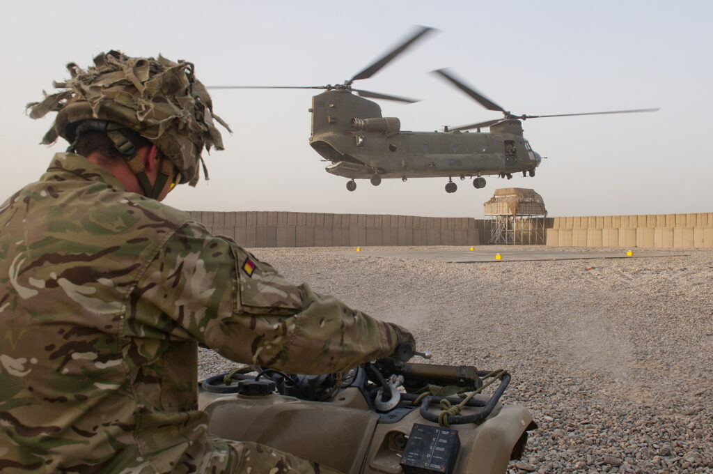 A soldier on a quad bike looks on as a Royal Air Force Chinook lands at Forward Operating Base Shawquat to drop off troops, post and supplies off at the base in Helmand Province, Afghanistan.