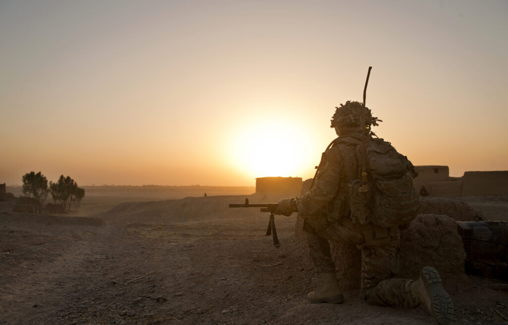 A soldier of 5 RIFLES kneels near the end of a patrol in Helmand, Afghanistan as the sun begins to set casting long shadows across the road. Only a matter of hours later the troops will be starting before dawn to begin their next patrol. In August 2014, 5 RIFLES and the Queen's Royal Hussars (QRH) completed the final operation to be carried out by the Warthog Group before Op Herrick ends later in the year. The operation, which concentrated on the Lashkar Gar area, was carried out to maintain security in the area surrounding Camp Bastion. The 5 RIFLES dismount were transported and offered strength in depth from the Warthog armoured vehicles by the QRH.